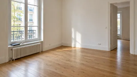 Pièce de location dégagée après retrait des meubles, mur et sol visibles près d’une fenêtre