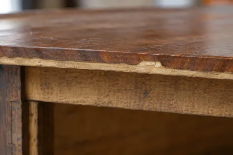 Détail d’un chant usé sur un meuble ancien, avec le support visible sous la surface