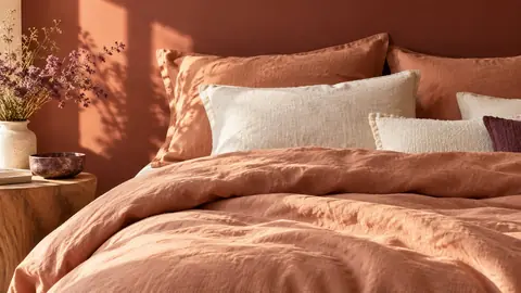 Linge de lit en lin terracotta clair devant un mur terracotta foncé